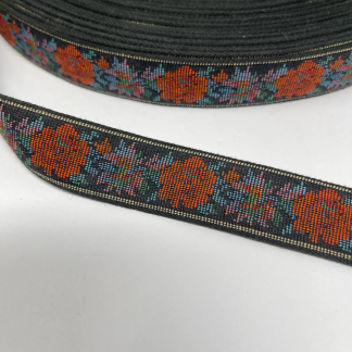 Close-up of vintage woven jacquard trim with orange and blue flowers on black, shown with ruler for scale.